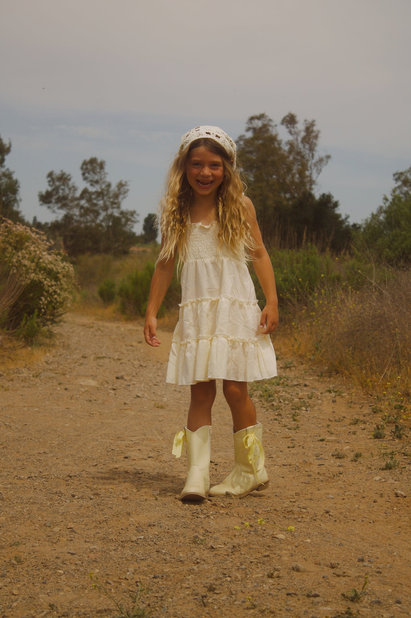 Little girl wearing a soft butter yellow cottagecore dress with flutter sleeves, posing outdoors in natural light. The dress has a vintage-inspired, dreamy feel—perfect for warm weather and whimsical adventures.