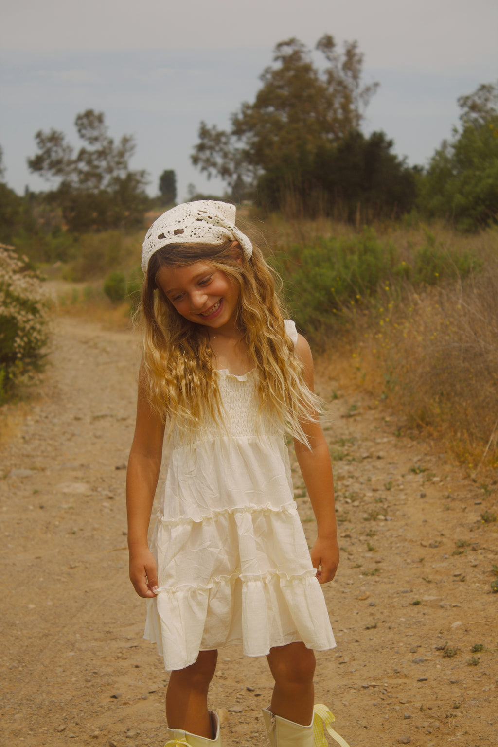 Little girl wearing a soft butter yellow cottagecore dress with flutter sleeves, posing outdoors in natural light. The dress has a vintage-inspired, dreamy feel—perfect for warm weather and whimsical adventures.