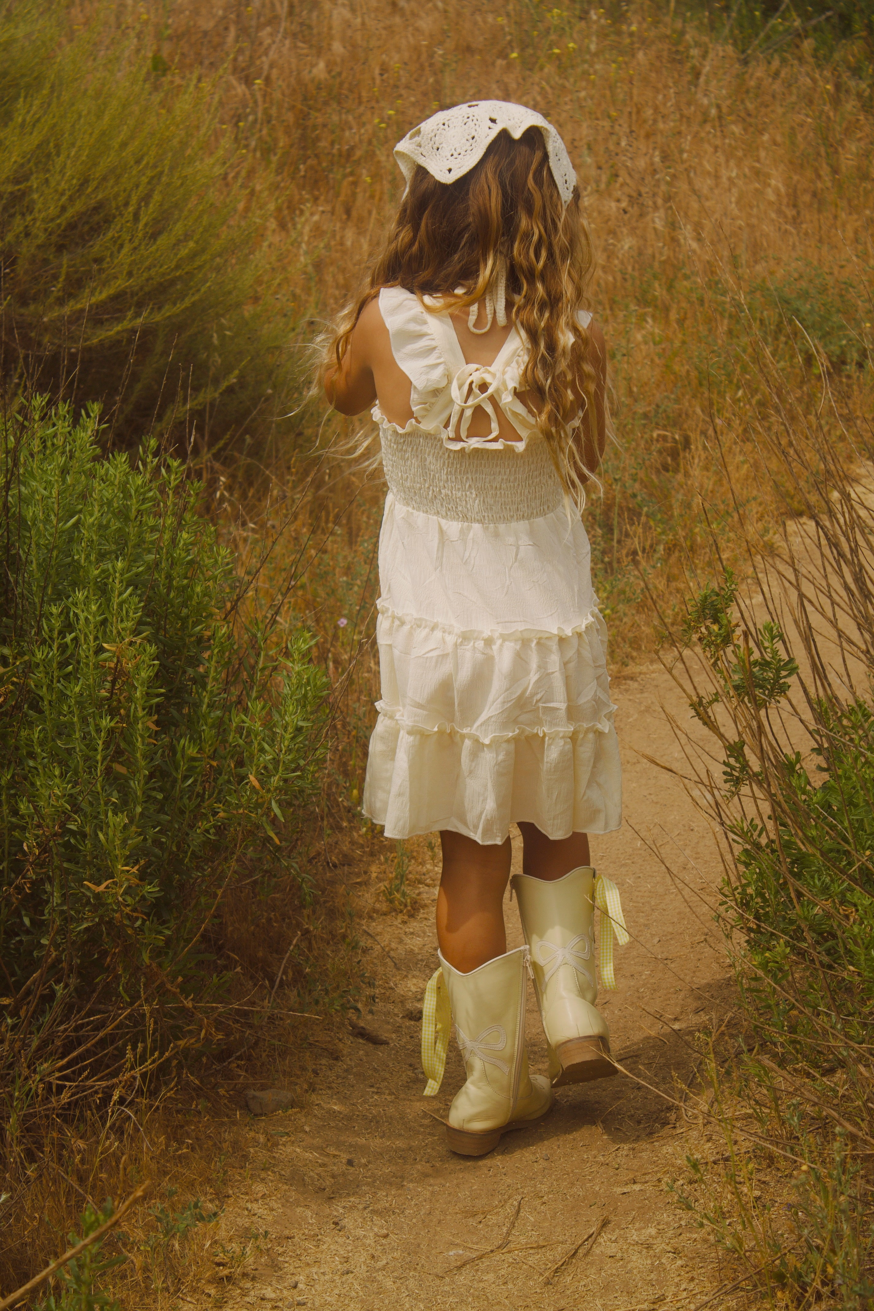 Little girl wearing a soft butter yellow cottagecore dress with flutter sleeves, posing outdoors in natural light. The dress has a vintage-inspired, dreamy feel—perfect for warm weather and whimsical adventures.
