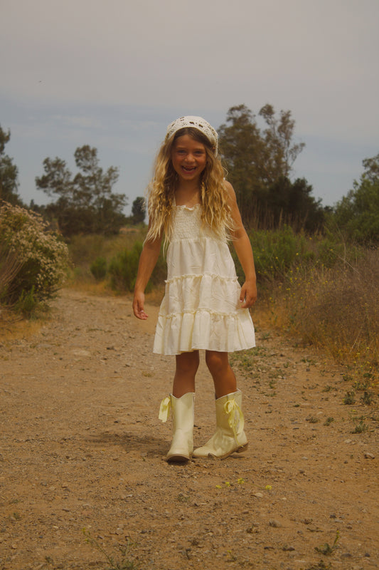 Little girl wearing a soft butter yellow cottagecore dress with flutter sleeves, posing outdoors in natural light. The dress has a vintage-inspired, dreamy feel—perfect for warm weather and whimsical adventures.