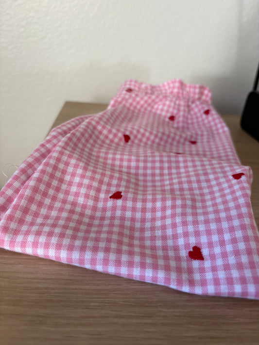Pink checkered fabric with red heart shapes on a white and wooden surface