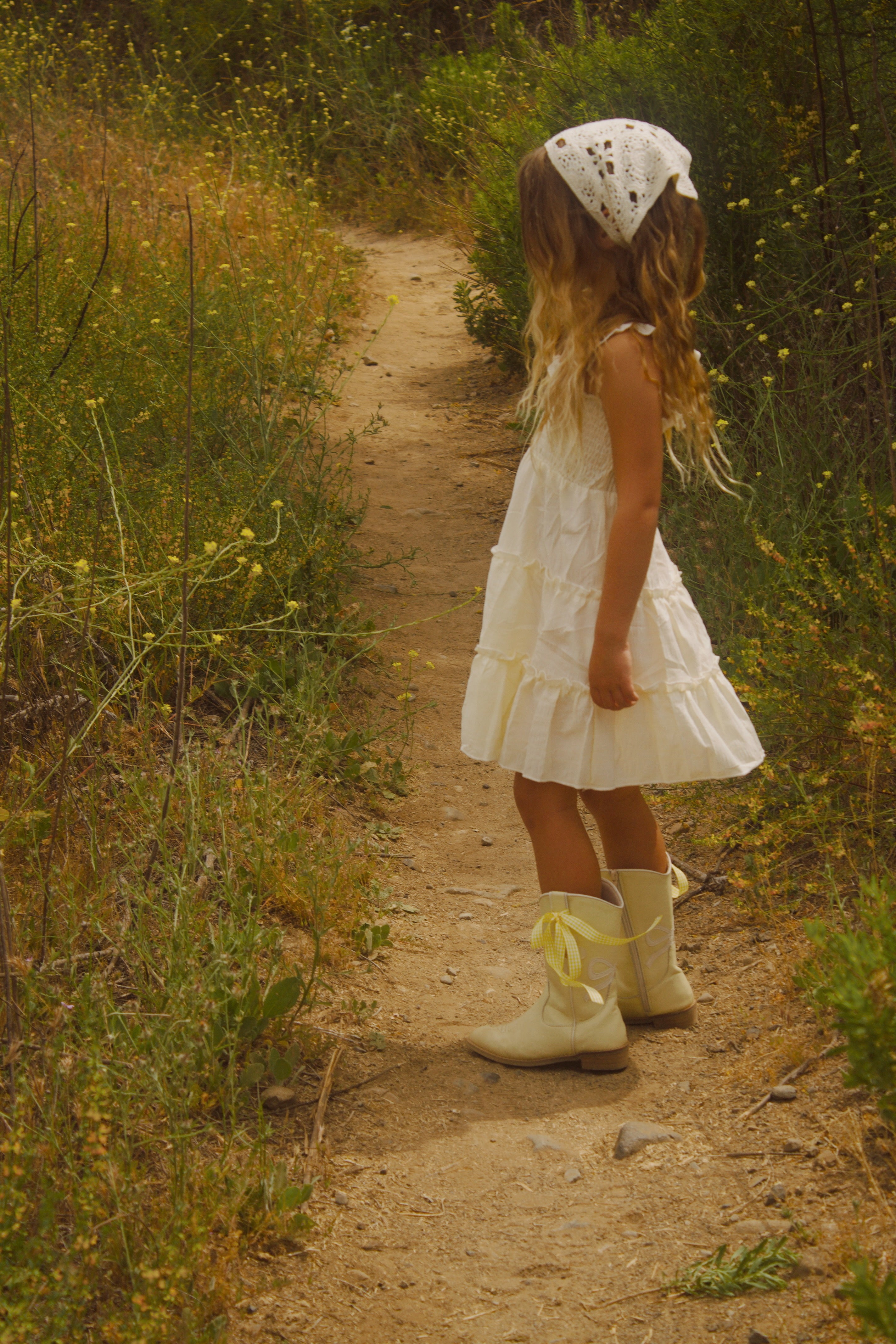 Little girl wearing a soft butter yellow cottagecore dress with flutter sleeves, posing outdoors in natural light. The dress has a vintage-inspired, dreamy feel—perfect for warm weather and whimsical adventures.
